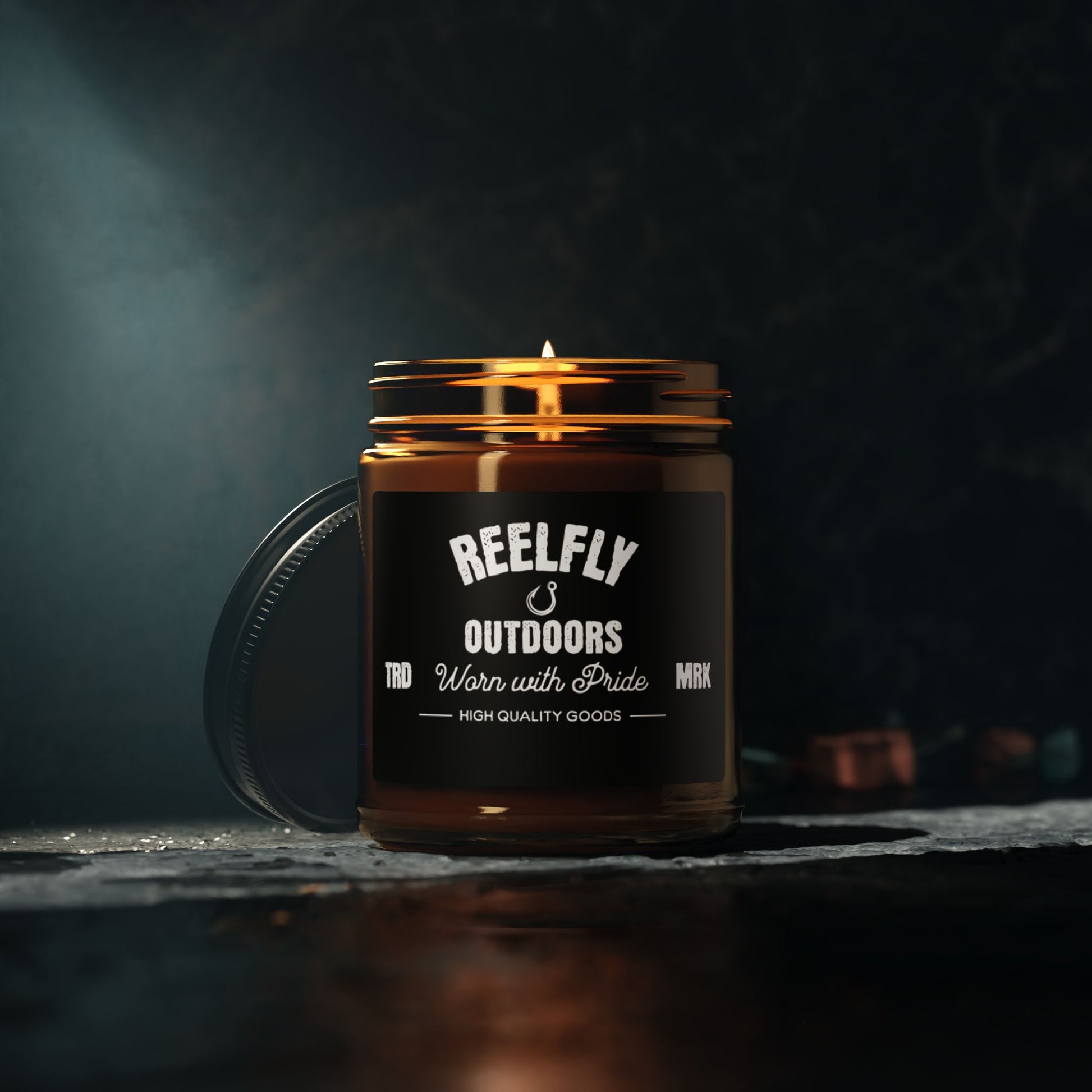 Reelfly Outdoors 9oz Trademark Candle sitting on table with dark surface in dim lighting